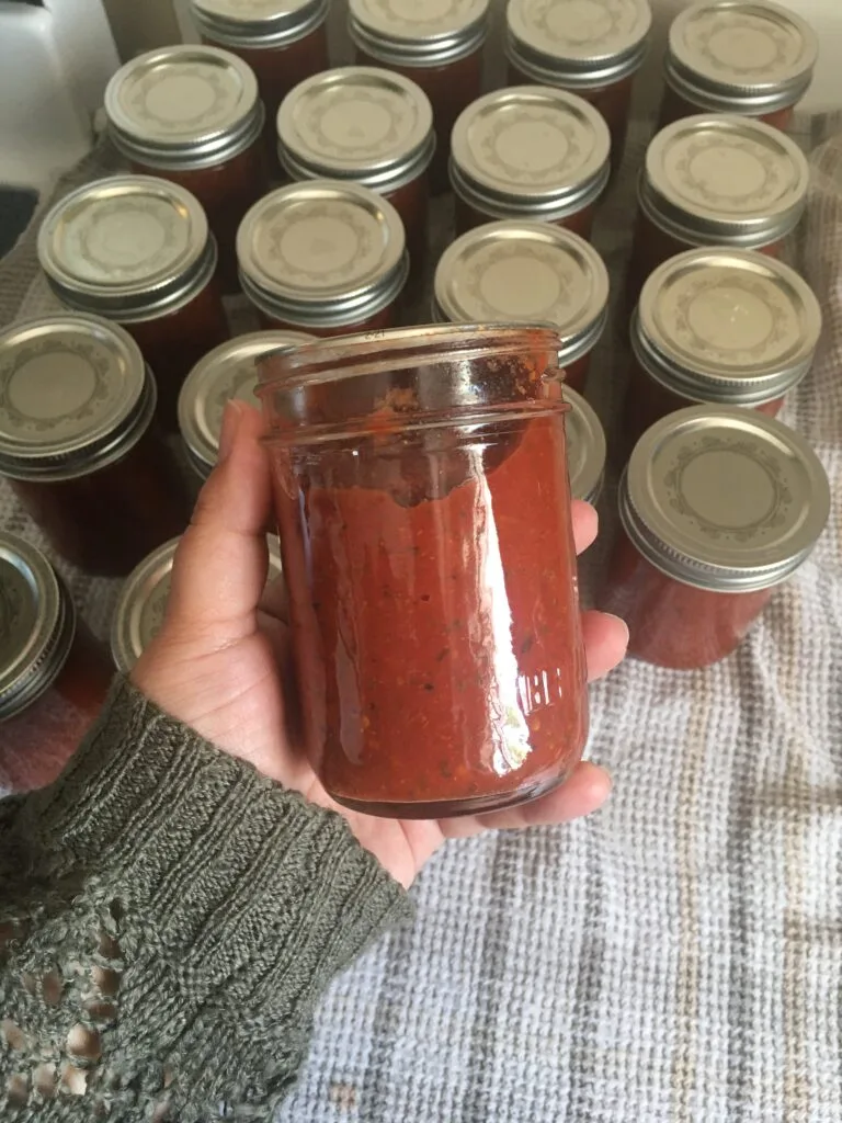 hand holding a pint sized mason jar filled with pizza sauce. more jars with lids visible in background.